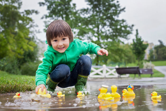 Little boy playing in puddle with rubber ducks